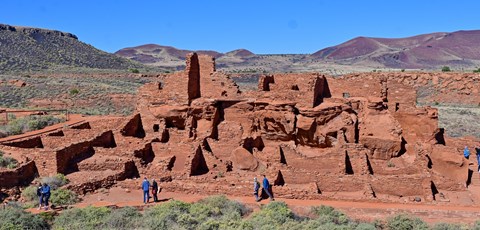 A large multi-room red sandstone pueblo with people walking in front