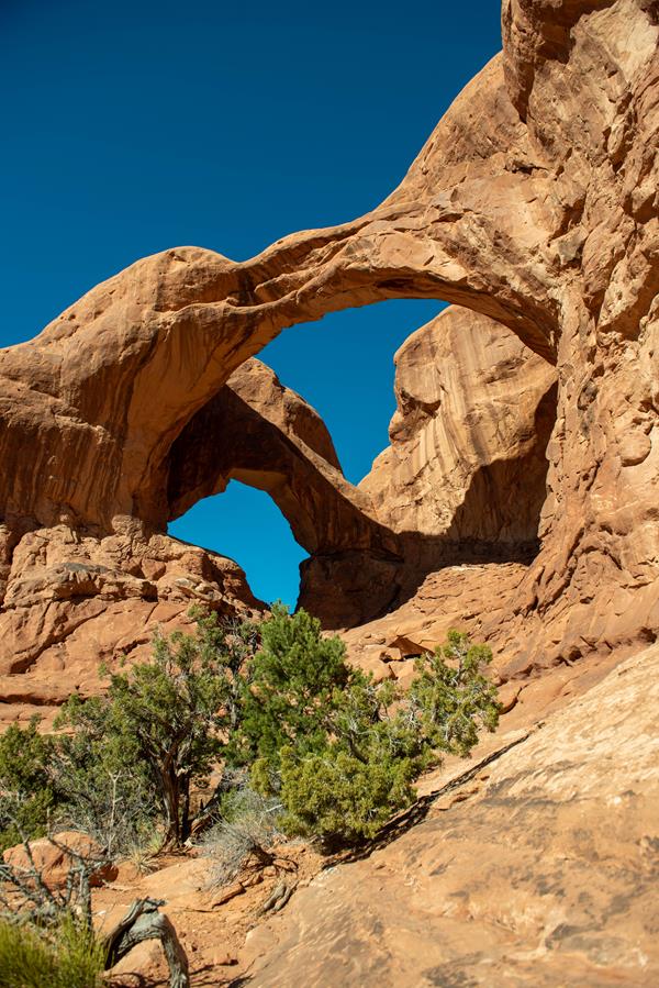Two sandstone arches connected on the left against a backdrop of blue sky.