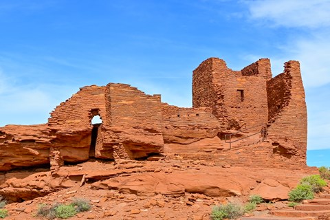 A red sandstone pueblo with a tower and three story tall wall