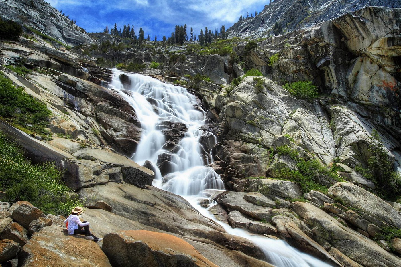A person sits on rounded rocks at the base of Tokopah Falls