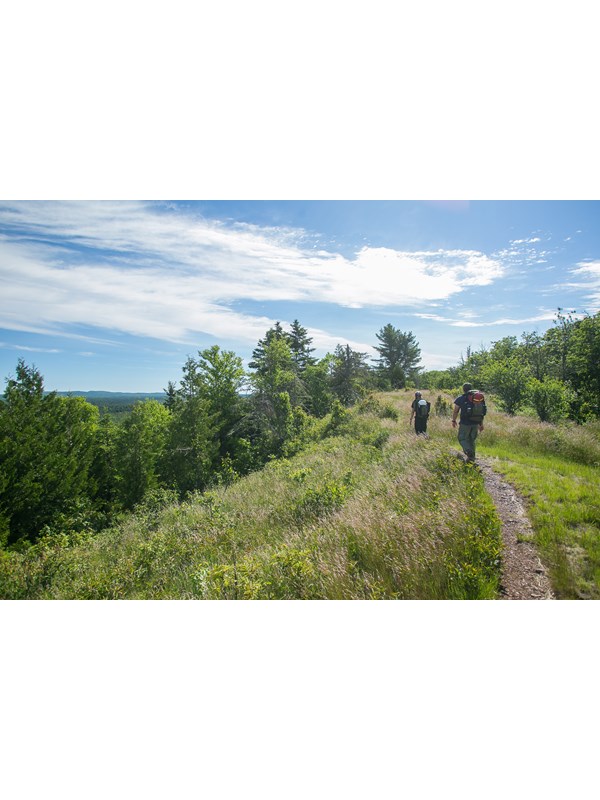 Two people with backpacks hike along a ridge top trail