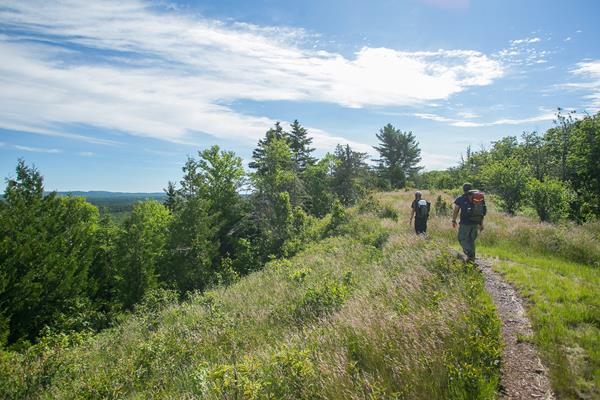 Two people with backpacks hike along a ridge top trail