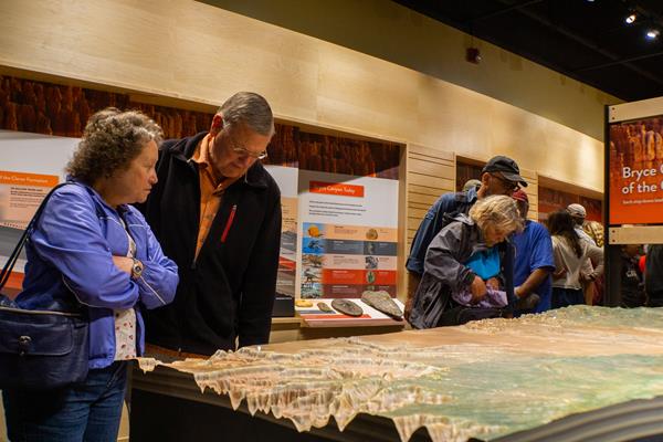 A couple stands among other people examining a relief map within the park museum