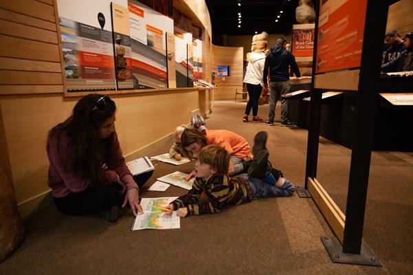 Three children and an adult sit on the floor working on an activity book