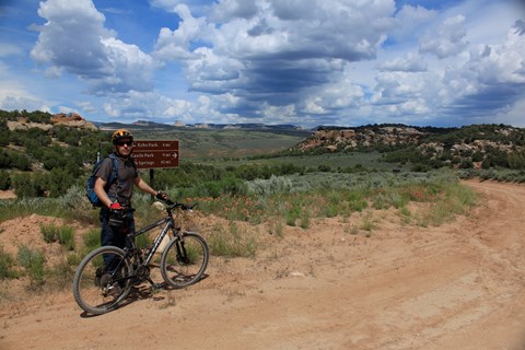 A man stands with a bike along a dirt road