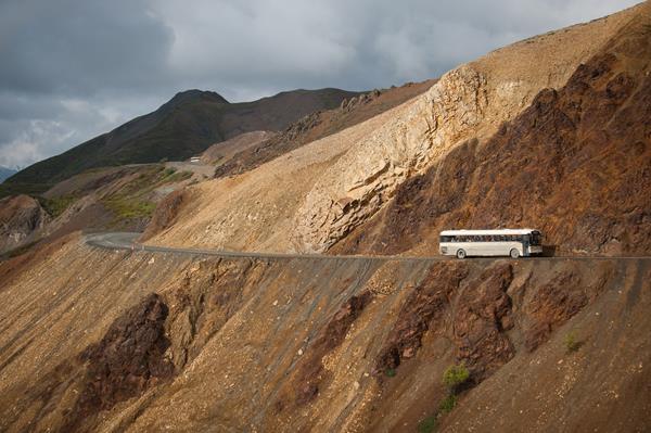 a bus driving on a dirt road on the side of a mountain