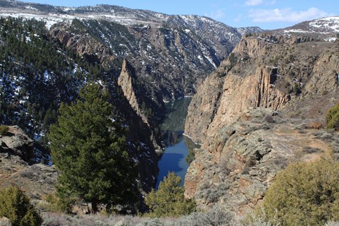 A deep steep canyon with a narrow body of water running far below. Snow is dusted on the canyon rim