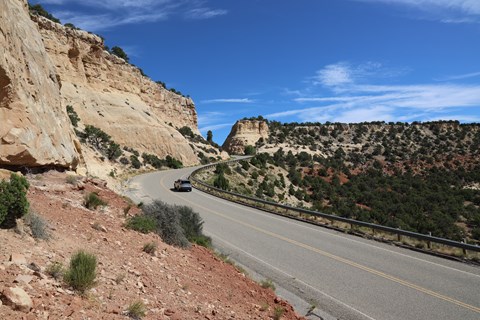 A card drives on a road that winds by yellow and red colored cliffs.