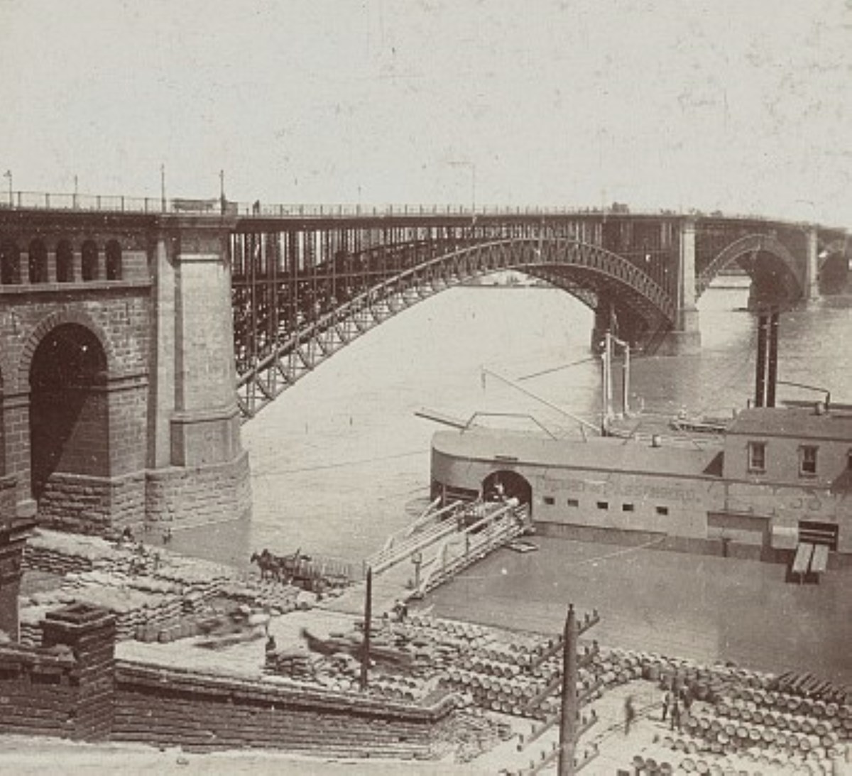 and old black and white photo of the Eads bridge with a boat and materials to be loaded stacked