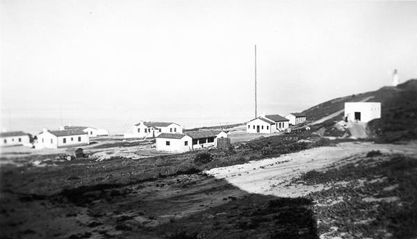 historic image of white buildings with tile roofs on ocean bluff.