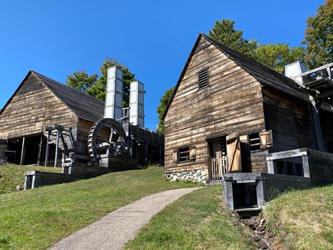 two wood-sided buildings with chimneys and water wheels under a bright blue sky