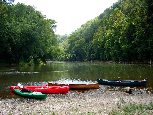 Canoes and kayaks sitting on the bank of a river.