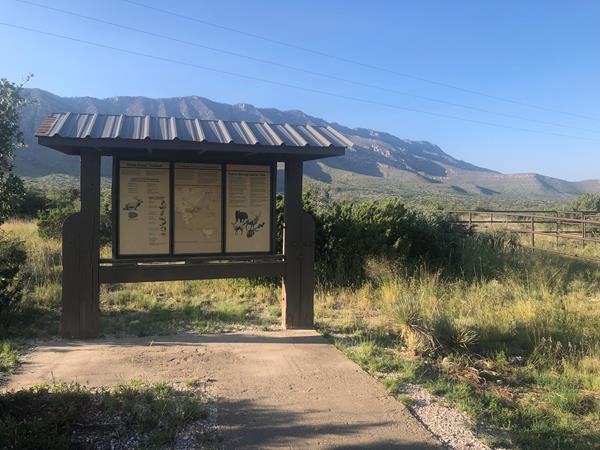 A wood kiosk with trail information in front of a desert mountain landscape