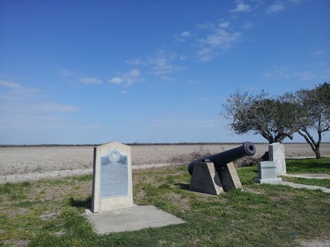 Concrete historical maker next to black siege cannon on concrete base.