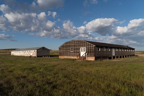 A historic mess hall and barracks sit in a grassy field at Minidoka.