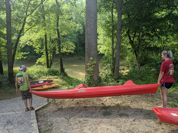 Two people carrying a red kayak down to the river