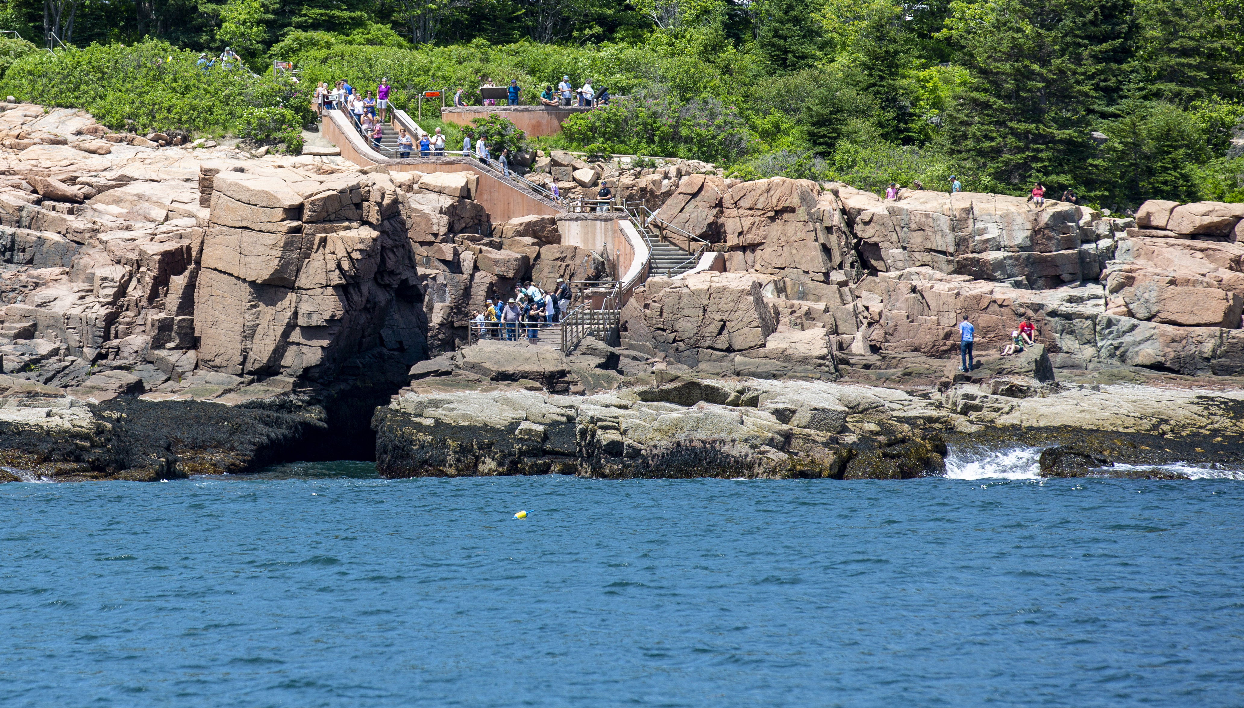 People gather on stairs leading down a cliff from a road to the ocean