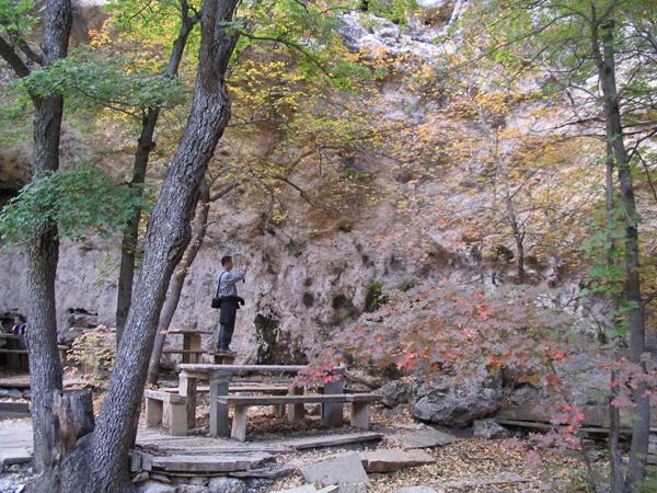 A man use a camera near an open cave feature with stone benches and tables.