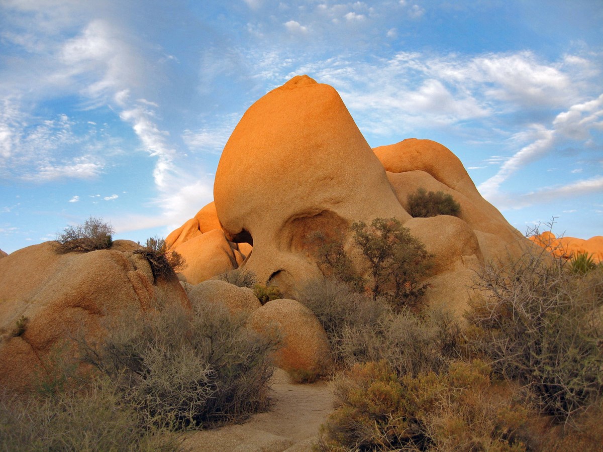 A large rock with two holes resembling eye sockets sticking out of a rock and boulder field.