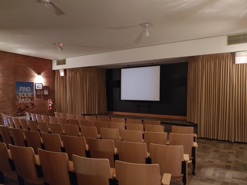 wooden chairs in row with a screen and a stage