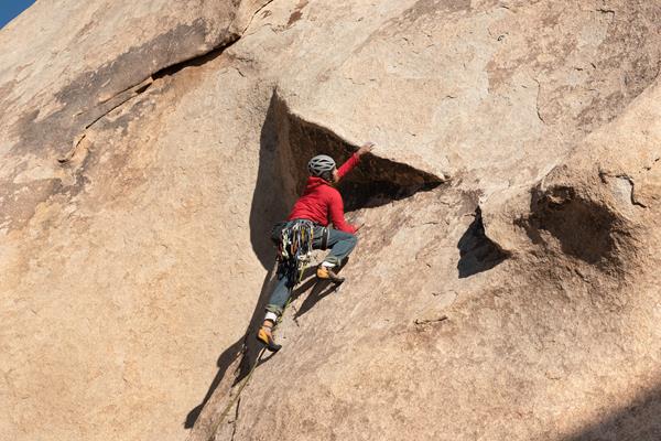 A rock climber making their way up a large reddish rock face.
