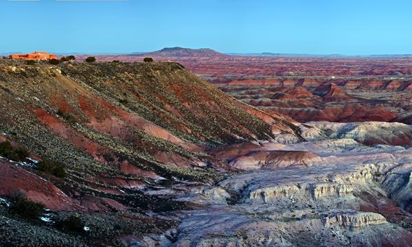 Overlooking white and red badlands from mesa edge at twilight, blue sky.