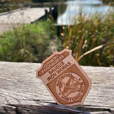 A wooden badge with the woods "Saugus Iron Works Junior Ranger"
