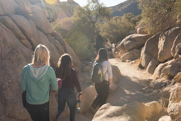 Three hikers walking along a dirt path running between large boulders.
