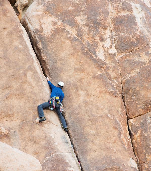 A rock climber making their way up a large reddish rock face.