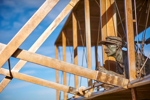 A bronze sculpture of Orville Wright surrounded by wooden beams of the flyer