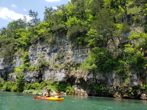 A yellow/orange canoe on a clear blue river with rock bluff in background
