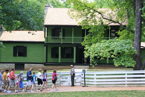 Park Ranger leading a large group of people towards the front gate of a green two-story house.