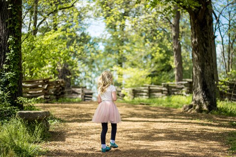 young girl walks on trail lined by a split-rail fence.