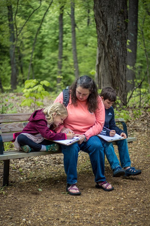 Mother and two children sitting on bench outside working on Junior Ranger book