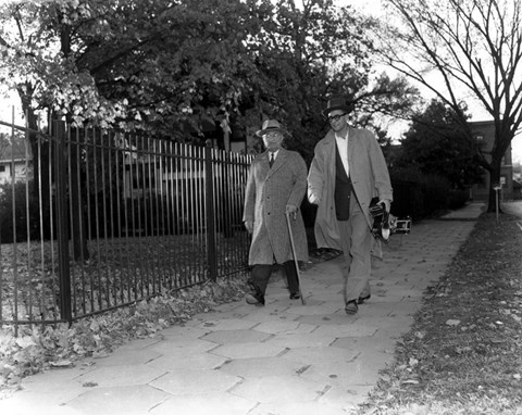 Harry S Truman, in coat and hat, with walking stick, walking.