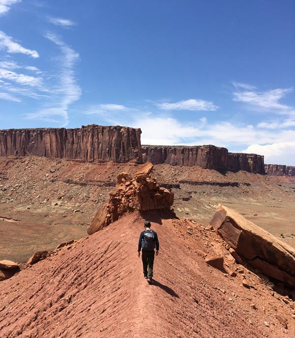 A hiker walks along a ridgeline towards Moses and Zeus Towers