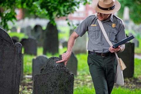 A park ranger points out something on a historic 18th century gravestone