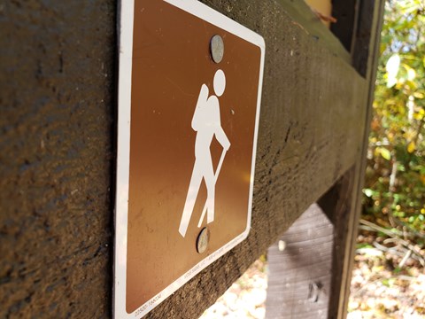 A brown sign up close on brown post with hiking emblem.
