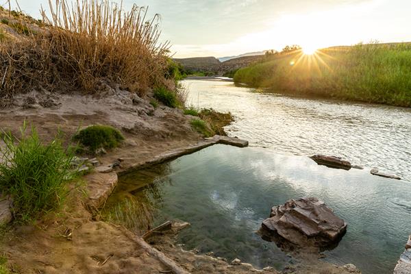 A pool of water encircled by a square rock foundation rises above a river.