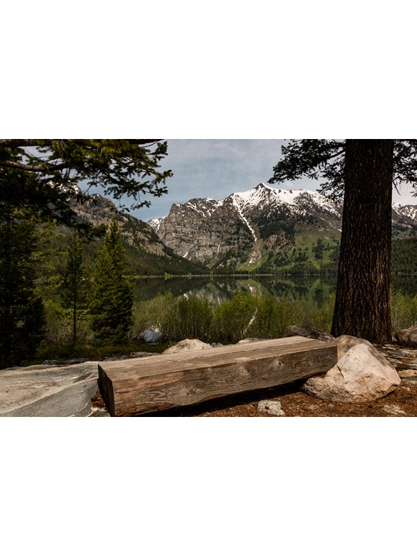 A wooden bench sits beside a lake surrounded by mountains.