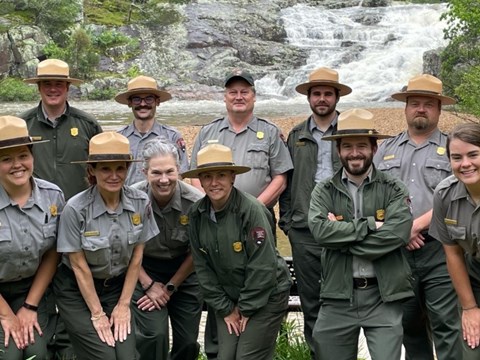 A group of National Park Service Rangers in uniform posing for a picture with a waterfall behind
