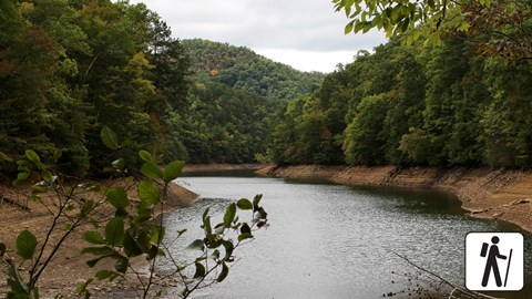 A small lake surrounded by trees and a rolling mountain in the background.