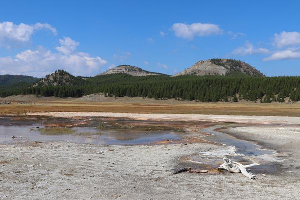 A thermal area sits in a meadow in front of rolling hills.
