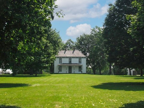 Large cream color farm home with green trim, grass and trees