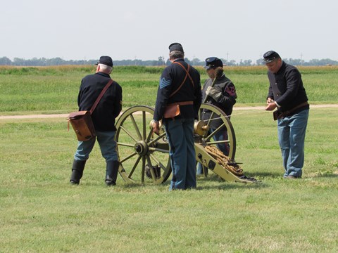 Men in 19th century U.S. Army uniforms prepare to fire a cannon.