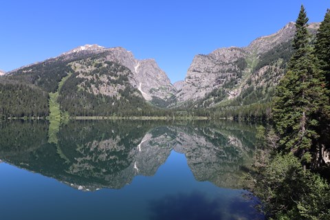 A lake sits at the base of a mountain canyon with a near perfect reflection on its calm surface.