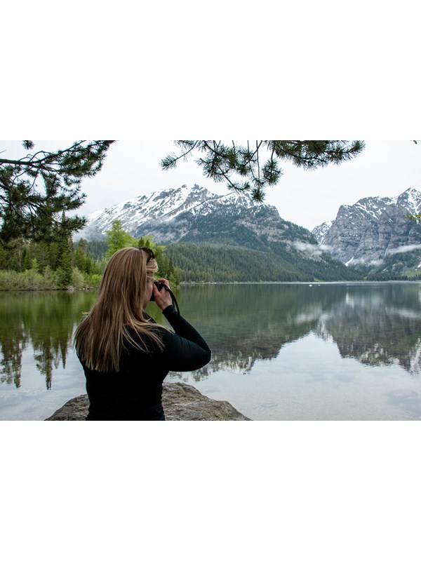 A woman takes a picture beside a lake.