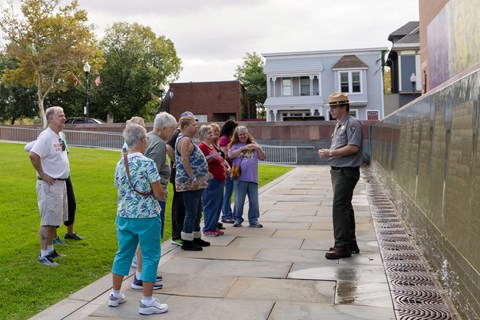 A ranger stands and speaks to a group of people in front of a wall.