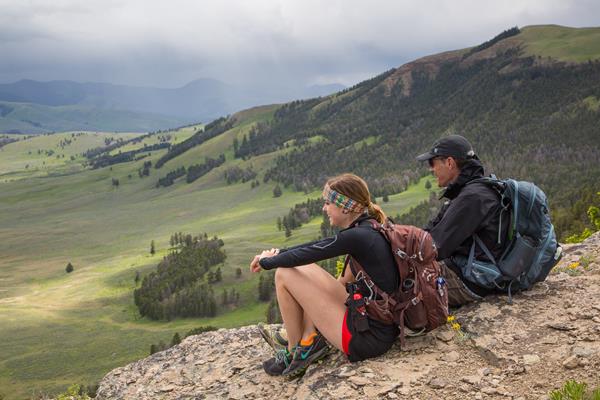 Two hikers sit on a ridgeline taking in views of the valley below.