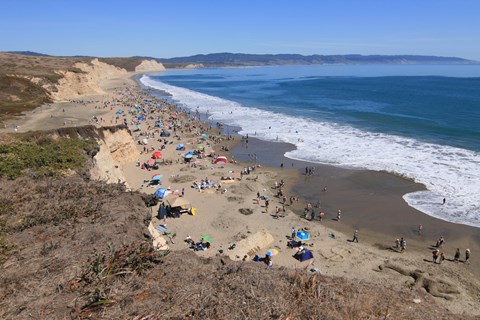 Looking down from a bluff top at a crowded sandy beach with some people swimming in the water.
